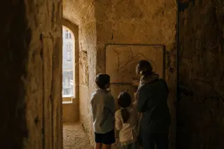 Family quietly examining a map together in a sunlit stone corridor inside Suze-la-Rousse castle, with soft afternoon light and an atmosphere of historical immersion.